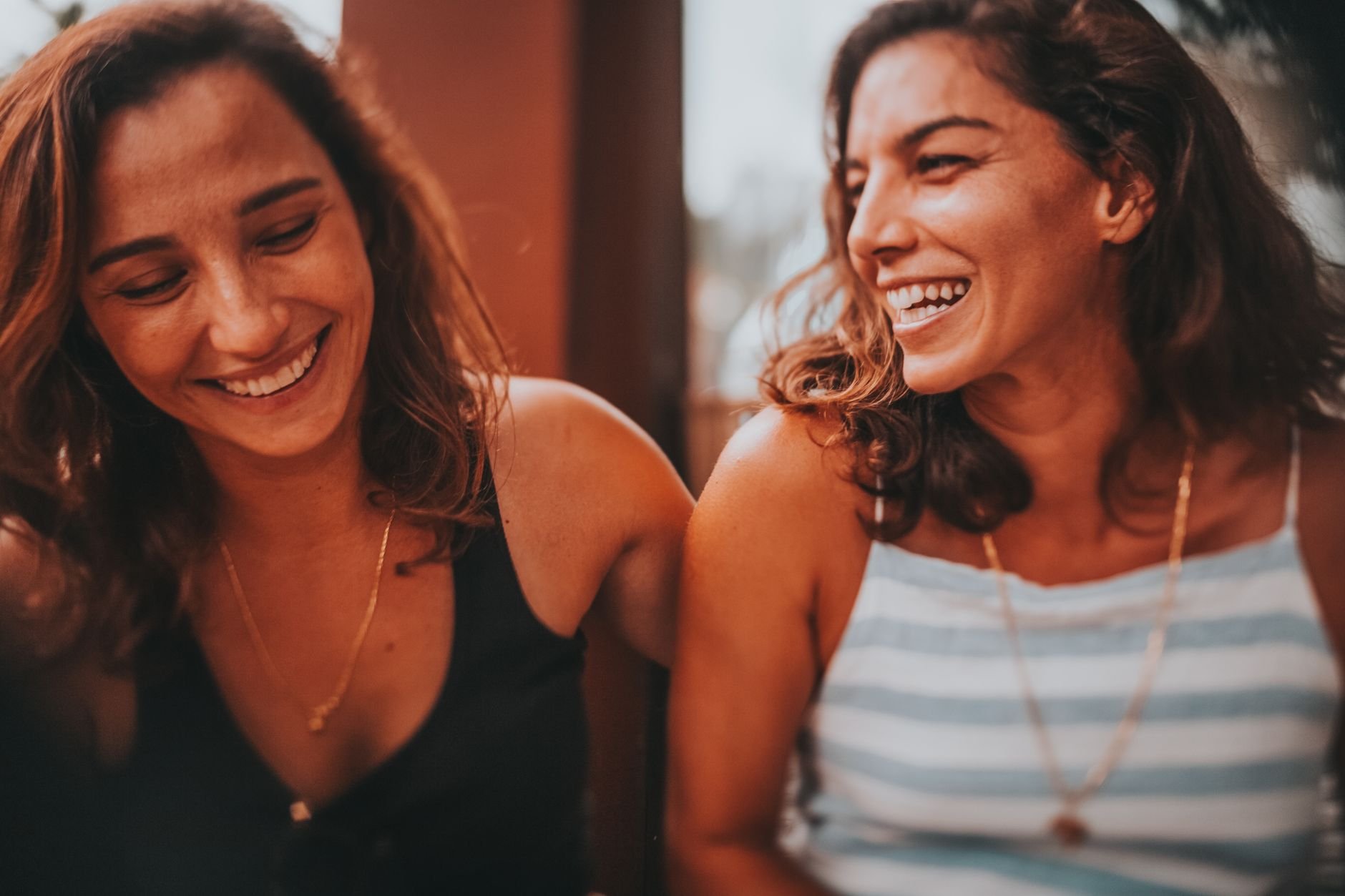 Two happy women laughing together outdoors, capturing a joyful moment in warm lighting.